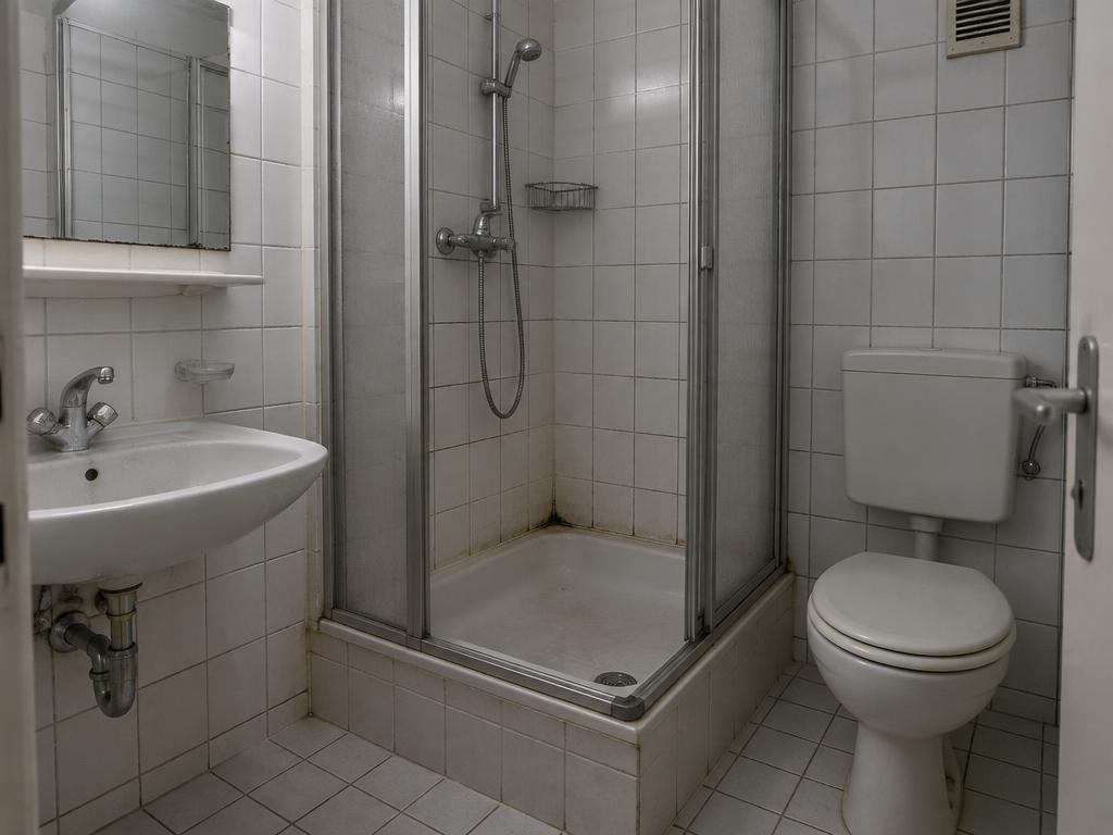 Altes Fliesenbad vor der Sanierung: hohe Duscheinstiegsstufe und unhygienische Fugen